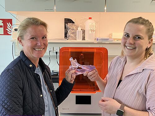 Dr. Nadja Engel und Laura Lembcke im Zelllabor der Mund-Kiefer-Gesichtschirurgie. Im Hintergrund der neu erworbene 3D-Drucker zur Herstellung von Modellen zur Implantatentwicklung. In der Hand ein Kiefermodell, das zu Simulationszwecken benötigt wird (Foto: Joachim Mangler).