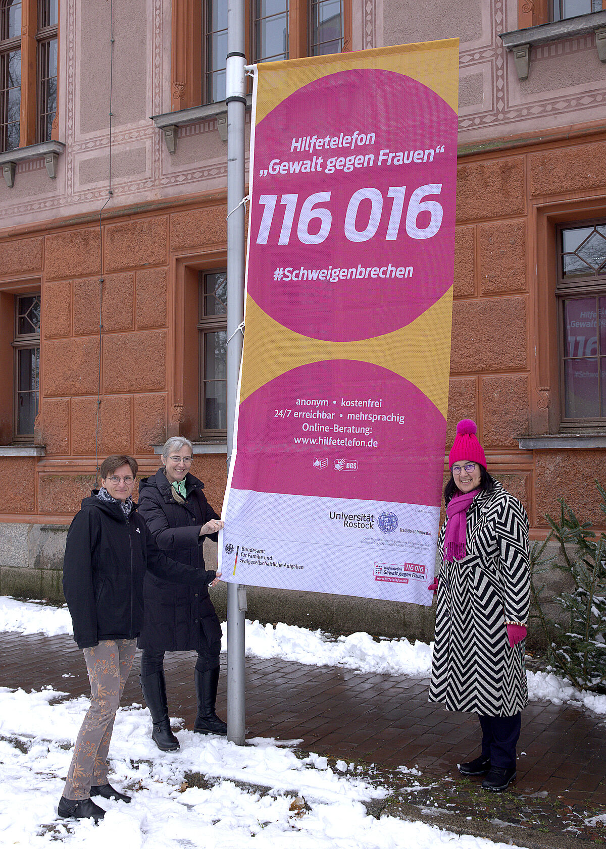 Dr. H. Jander, Prof. Dr. N. Wrage-Mönnig und Rektorin Prof. Dr. E. Prommer (v.l.) neben der gehissten Fahne mit der Nummer des Hilfetelefons. (Julia Tetzke/Universität Rostock)