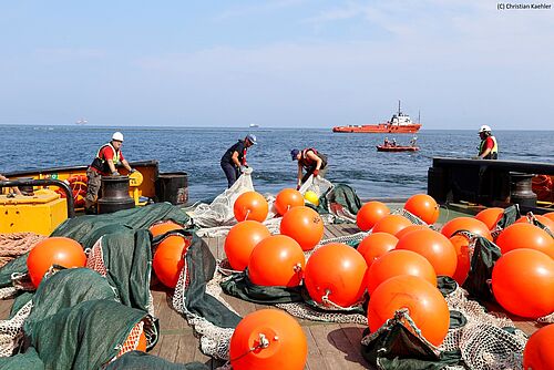 Mitarbeiter der Universität Rostock und Universität Stettin bringen mit Mitarbeitern der polnischen Seenotrettung die Netzsperre für eine Übung aus. Sie befinden sich dabei auf dem Schiff „Kapitan  Poinc“, das von Polish Search and Rescue zur Ölhavariebekämpfung eingesetzt wird. Im Hintergrund eine Ölbohrinsel, ein Öltanker (Mitte) und das Multifunktionsschiff „Bazalt“, das gerade eine Ölsperre zu Übungszwecken auslegt. 