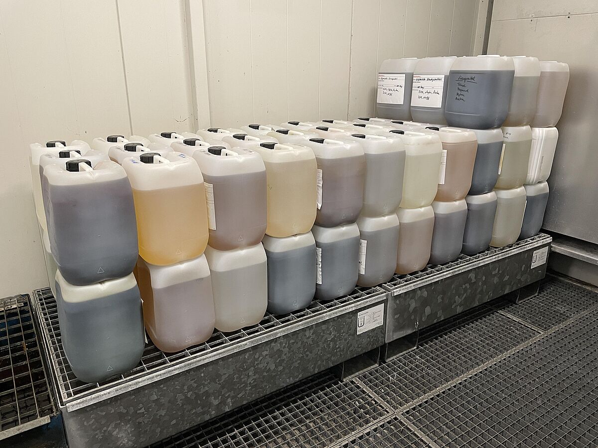 Das Foto zeigt eine Aufreihung von 10 L Kanistern, den mit verschiedenfarbigen organischen Lösemittelabfällen gefüllt sind.