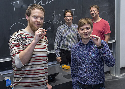 Lucas Teuber und Mark Kremer präsentieren stolz die Glasplatten mit den eingavierten Wellenleitern. Im Hintergrund (v.l.) Professor Stefan Scheel und Professor Alexander Szameit