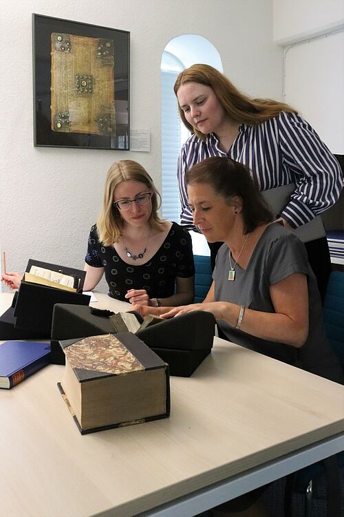 Part of the relevant literature is available in the special collection of the university bookstore, where Franziska Schreiber, Professor Stephanie Wodianka (from left) and Julia Borzinski (standing) are researching (Photo: Anna Fröhlich).
