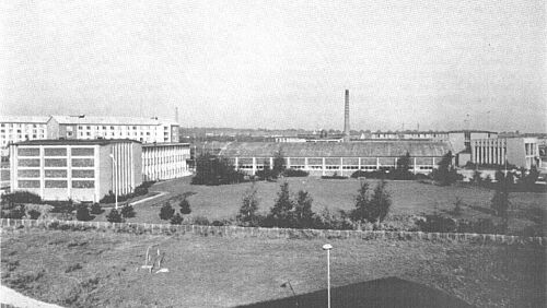 Das Foto zeigt das Sektionsgelände 1971. Vermutlich aus einem der Hochhäuser in der Rostocker Schlesinger Straße aufgenommen. Von links nach rechts: Statikhalle mit Statikgebäude, Strömungshalle, Großer Hörsaal. Den Schornstein gibt es nicht mehr. 