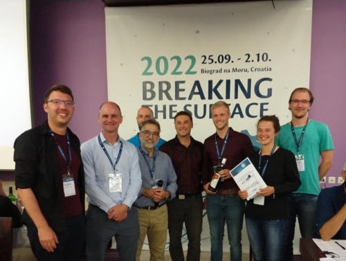 Das Team aus Rostock (ganz links: Ian Karez; von rechts nach links: Sven Lack, Greta Markfort und Johannes Marx, hier auf dem Foto zusammen mit der Jury) holte sich mit seiner innovativen Unterwasserlokalisierung den ersten Platz (Foto: Lehrstuhl Regelungstechnik). 