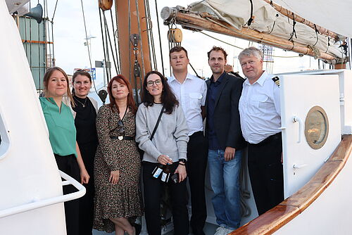 Elisabeth Reich und Friederike Feldmann (International Office Rostock), Ana Timonina-Mickevičienė (Klaipeda University), Andrea Ruth (Language Center Rostock), Antanas Gerasimavičius (2nd Officer), Gintautas Minelga (1st Officer) sowie Joseph Herbst (EU-CONEXUS) stehen gemeinsam an Bord des Forschungsschiffs für ein Gruppenfoto.