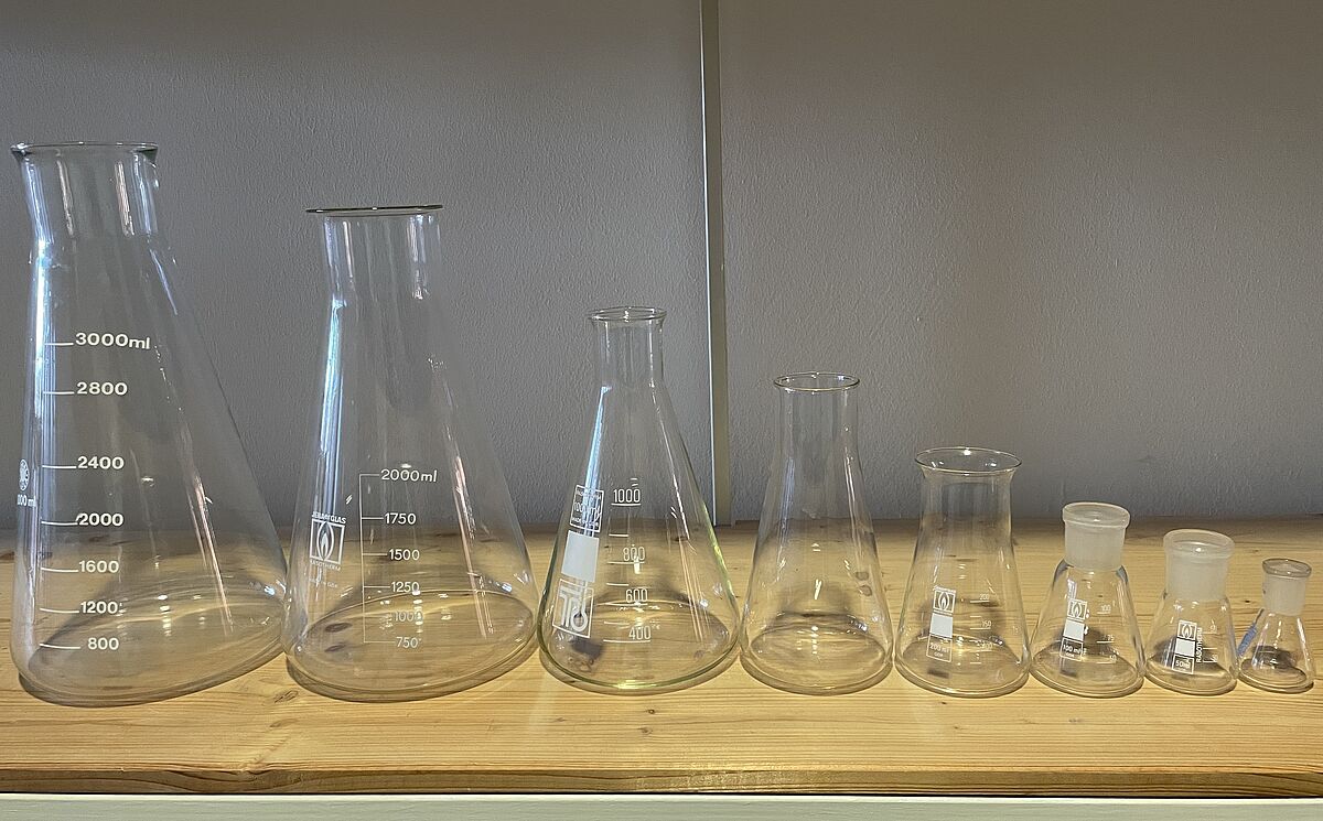Ein Foto aus dem Glaslager im Entsorgungshof der Universität Rostock. Das Foto zeigt eine Reihe von Erlenmeyerkolben, sortiert nach Größe, von 25 Milliliter bis 3 Liter.